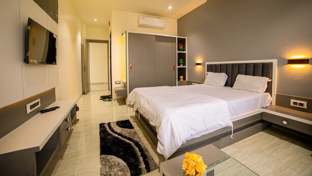 A modern bedroom with a bed, bedside tables, a TV, and a built-in wardrobe. - Hotel KV Pride (Mehekar)