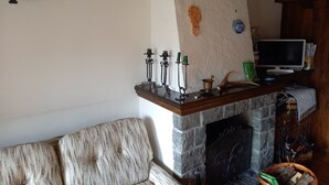 Ein gemütliches Wohnzimmer mit Kamin, einer Holzregal mit Kerzen, einem Fernseher und einem gemusterten Sofa.
