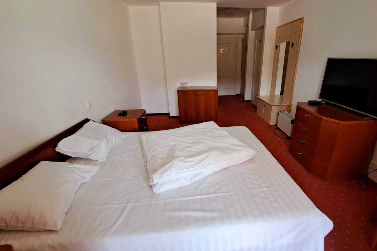 A hotel room with a bed, a TV, a dresser, and a small table.