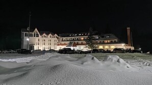 A large, multi-story building with a symmetrical facade, illuminated windows, and a prominent chimney. - Hotel Iadolina (Budureasa)
