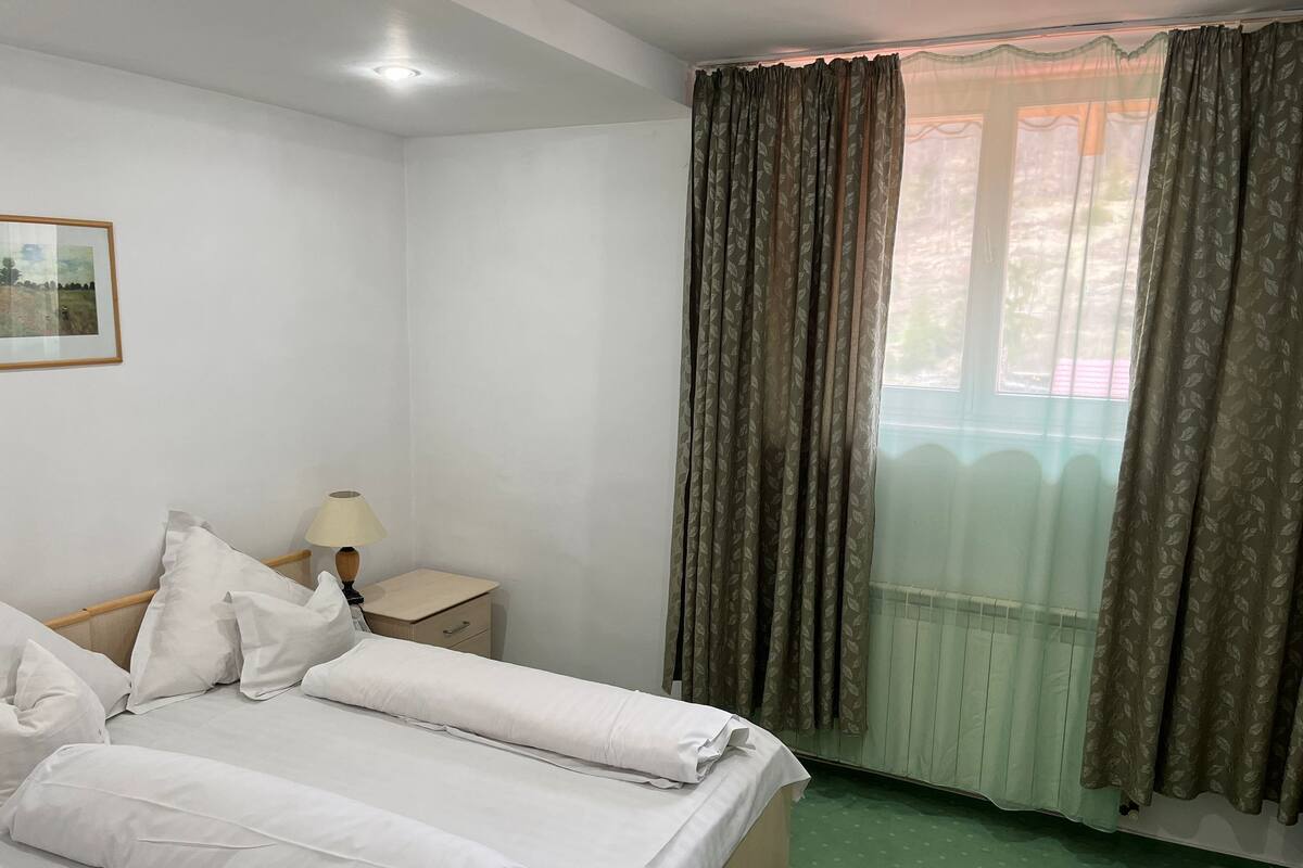A neatly made bed with white linens, a bedside lamp, and a small bedside table with a drawer.