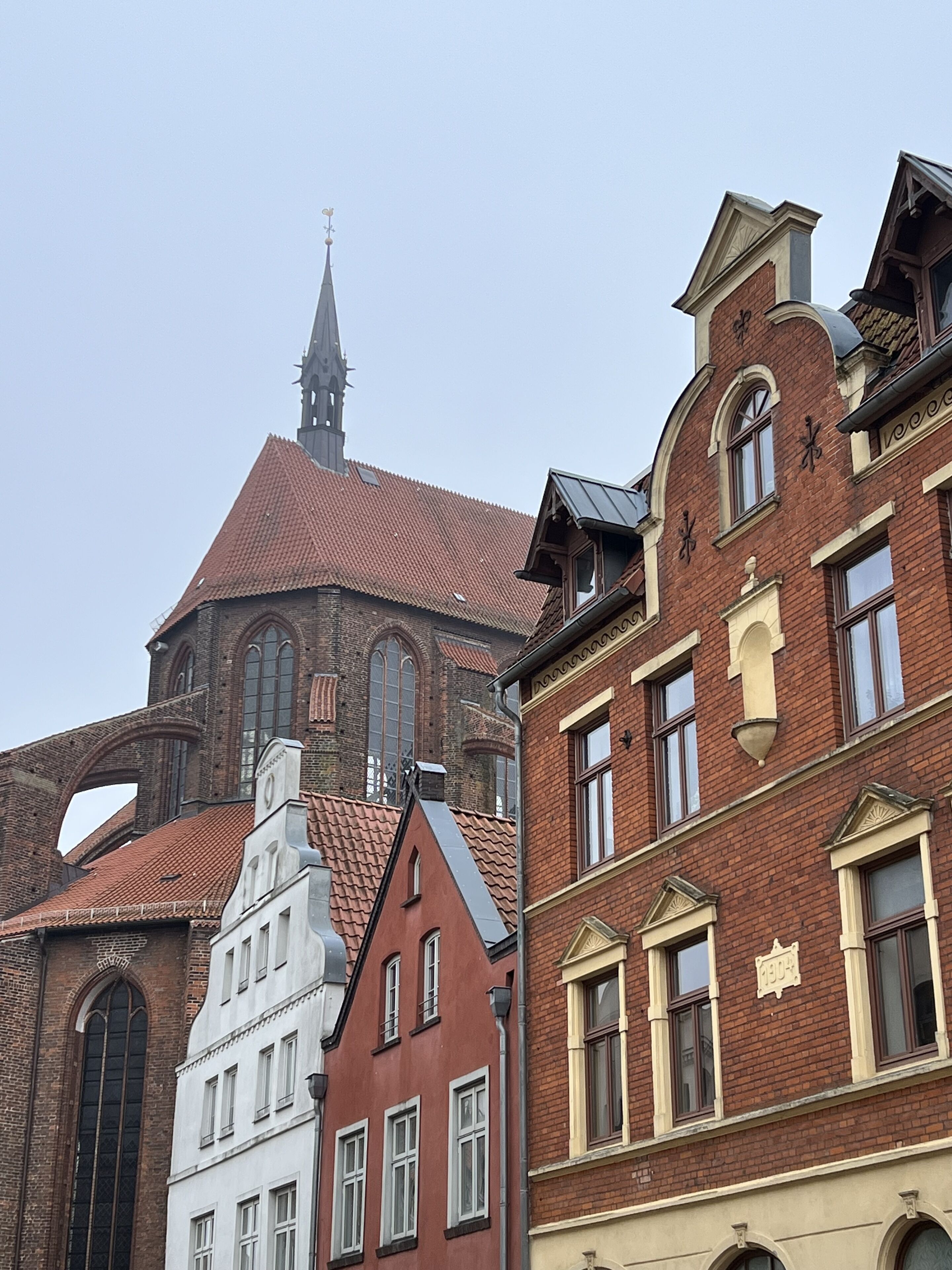 A historic building with a prominent tower and a church steeple in the background.