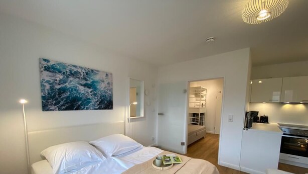 Une chambre à coucher avec un lit, des tables de chevet, une commode, un tableau et une vue sur la cuisine.