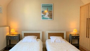 Quarto de hotel com duas camas de solteiro, cabeceiras de madeira, mesas de cabeceira com luminárias, um quadro na parede e um guarda-roupa de madeira.