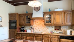 Uma cozinha com armários de madeira, um relógio, um fogão, uma pia e uma mesa de jantar com cadeiras.