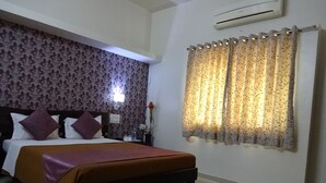 A hotel room with a bed, a nightstand, a wall-mounted air conditioner, and patterned curtains.