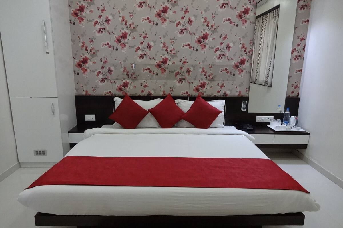 A bedroom with a bed, red pillows, a bedside table with a phone, and a mirror.