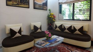 A living room with a sofa set, a glass coffee table, and two wall-mounted paintings.