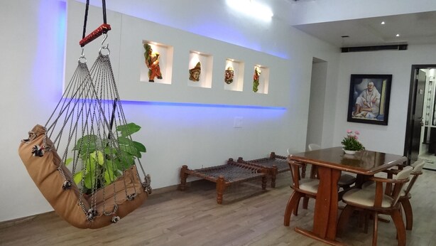 A dining area with a wooden table and chairs, a hanging chair with a plant, and wall-mounted decorative items.