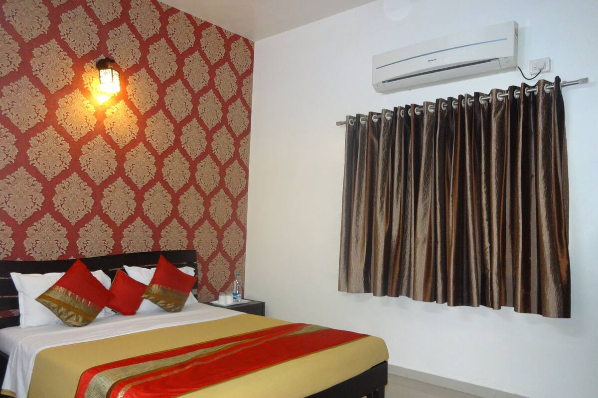 A hotel room with a bed, a nightstand, an air conditioner, and a curtain.