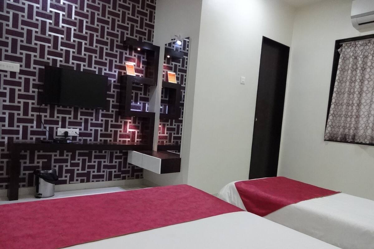 A hotel room with a patterned wall, a flat-screen TV, a small desk with a chair, and two beds with red and white bedding.