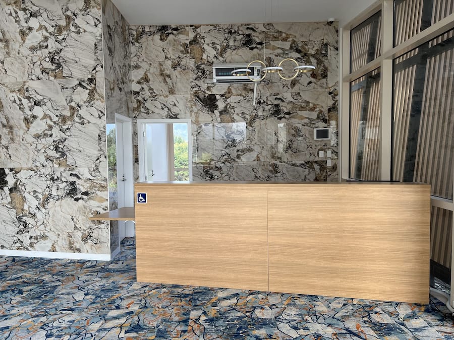 Un área de recepción con pared de mármol, mostrador de madera y piso con diseño.