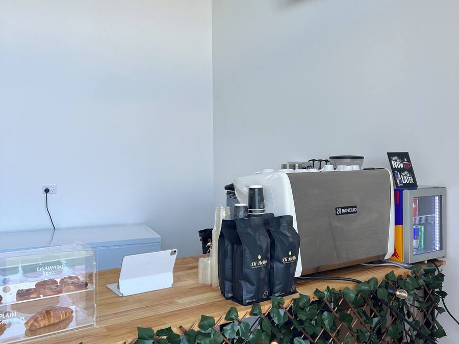 A coffee station with a coffee machine, bags of coffee, and a display case with pastries.