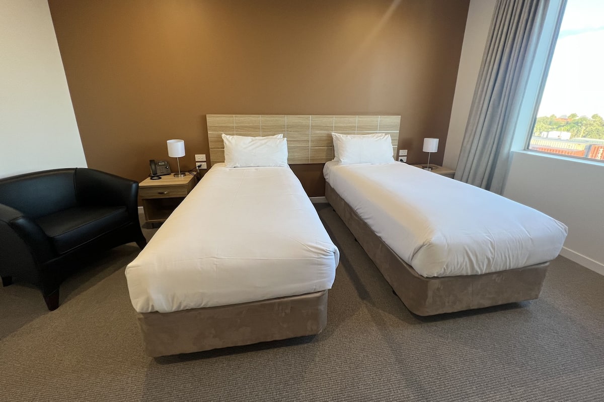 A hotel room with two beds, a desk, a chair, and a window with a view.