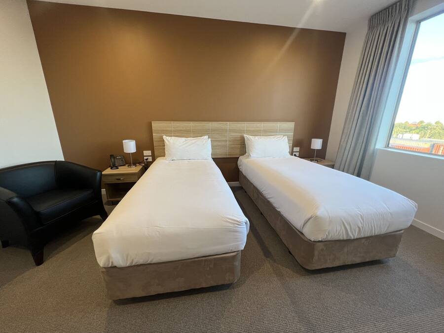 A hotel room with two beds, a desk, a chair, and a window with a view.