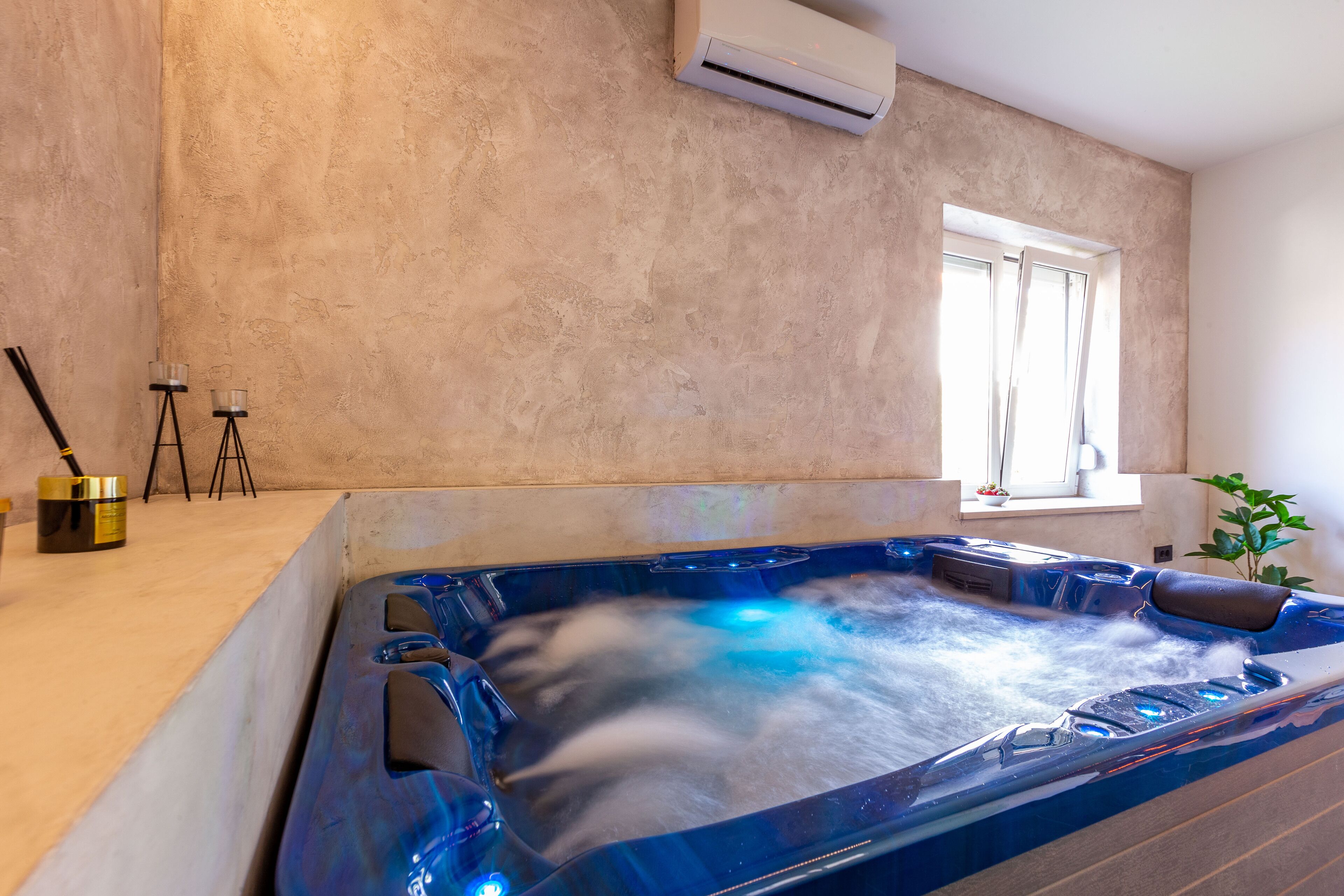 Een moderne badkamer met een ruime badkuip, een raam en een wandairconditioner.