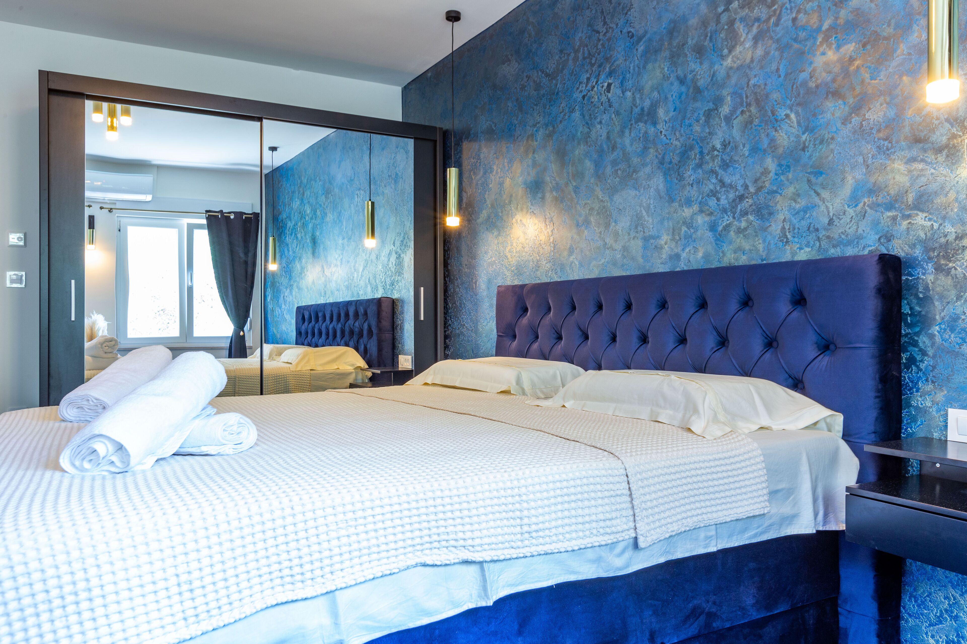 Un dormitorio moderno con una cama grande, un espejo y una pared azul con textura.