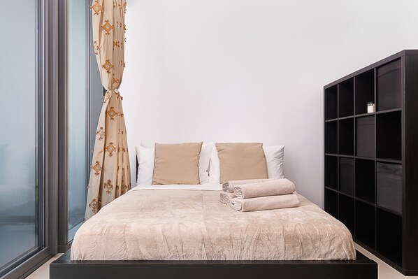 Una cama bien hecha con ropa de cama color beige, un cabecero negro y una ventana con cortinas.