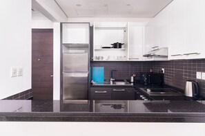 Une cuisine moderne avec un réfrigérateur en acier inoxydable, des plans de travail noirs et un pare-feu bleu.