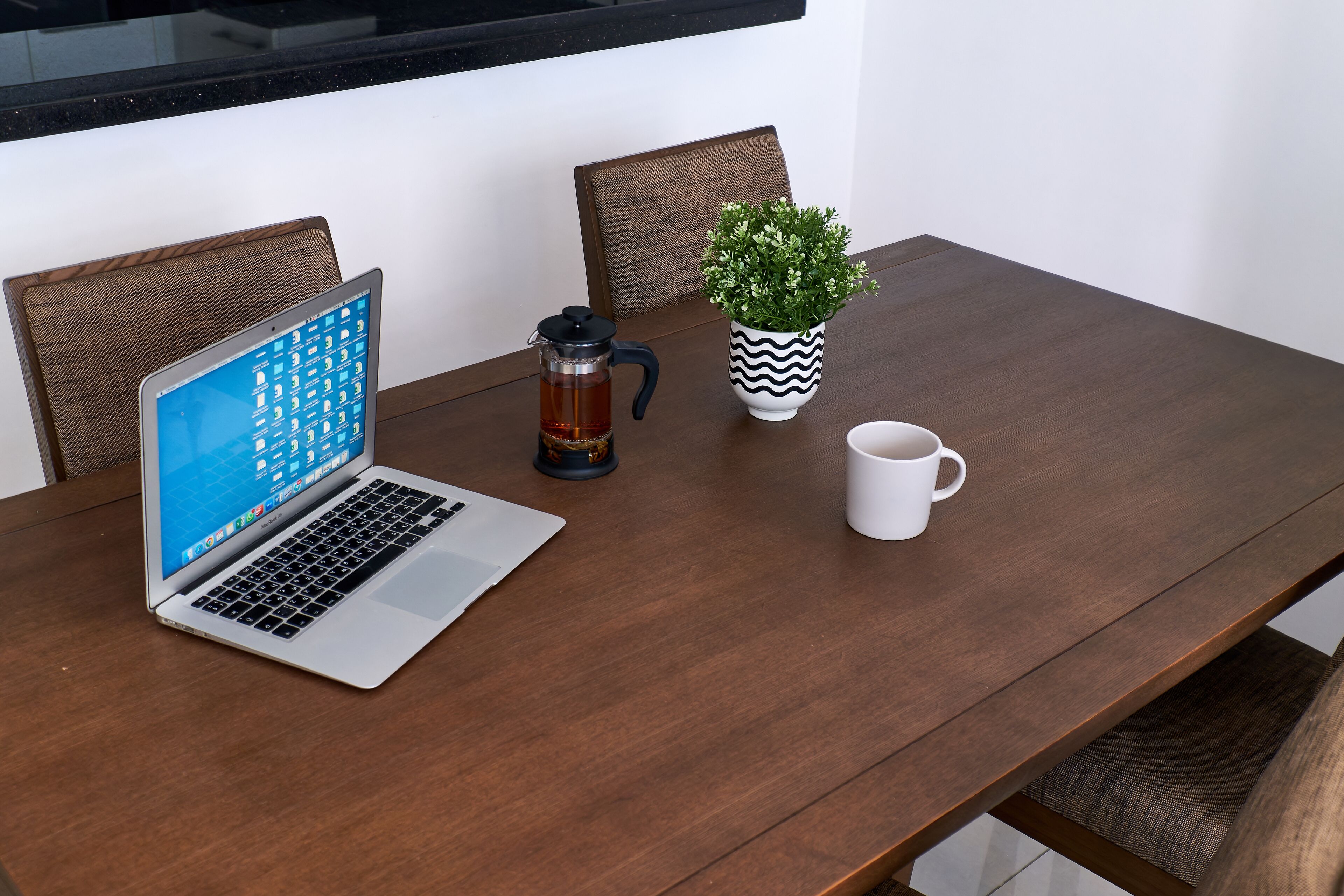 Un ordinateur portable est posé sur une table en bois, avec une machine à café et une plante en pot à côté.