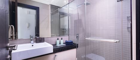 Un baño moderno con cabina de ducha de vidrio, un lavamanos blanco y un inodoro.