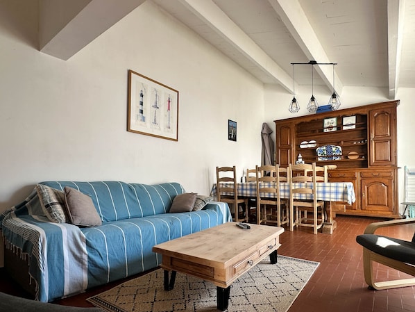 A living room with a blue-striped sofa, wooden coffee table, dining table with chairs, and a wooden cabinet with shelves.