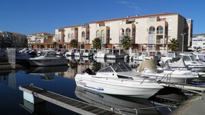 A marina with several boats docked, a wooden dock, and a building with multiple balconies in the background. - Bright 4-room apartment with balcony in Sète (Sète)