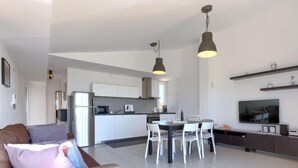 A modern living room with a sofa, dining table, and chairs. There is a kitchen area with cabinets and appliances. - Apartment Rak by Interhome (Umag/Zambratija)