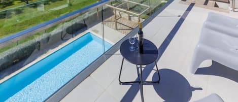 A balcony with a glass railing overlooking a swimming pool and a view of the sea.