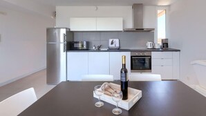 A modern kitchen with white cabinets, a built-in oven, and a dining table set with wine glasses and a bottle. - Apartment Rak by Interhome (Umag/Zambratija)