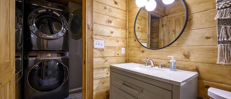 Un baño pequeño con paredes de madera, un lavabo con espejo y dos lavadoras apiladas.