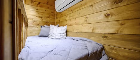 A single bed with a grey duvet in a wooden cabin room.