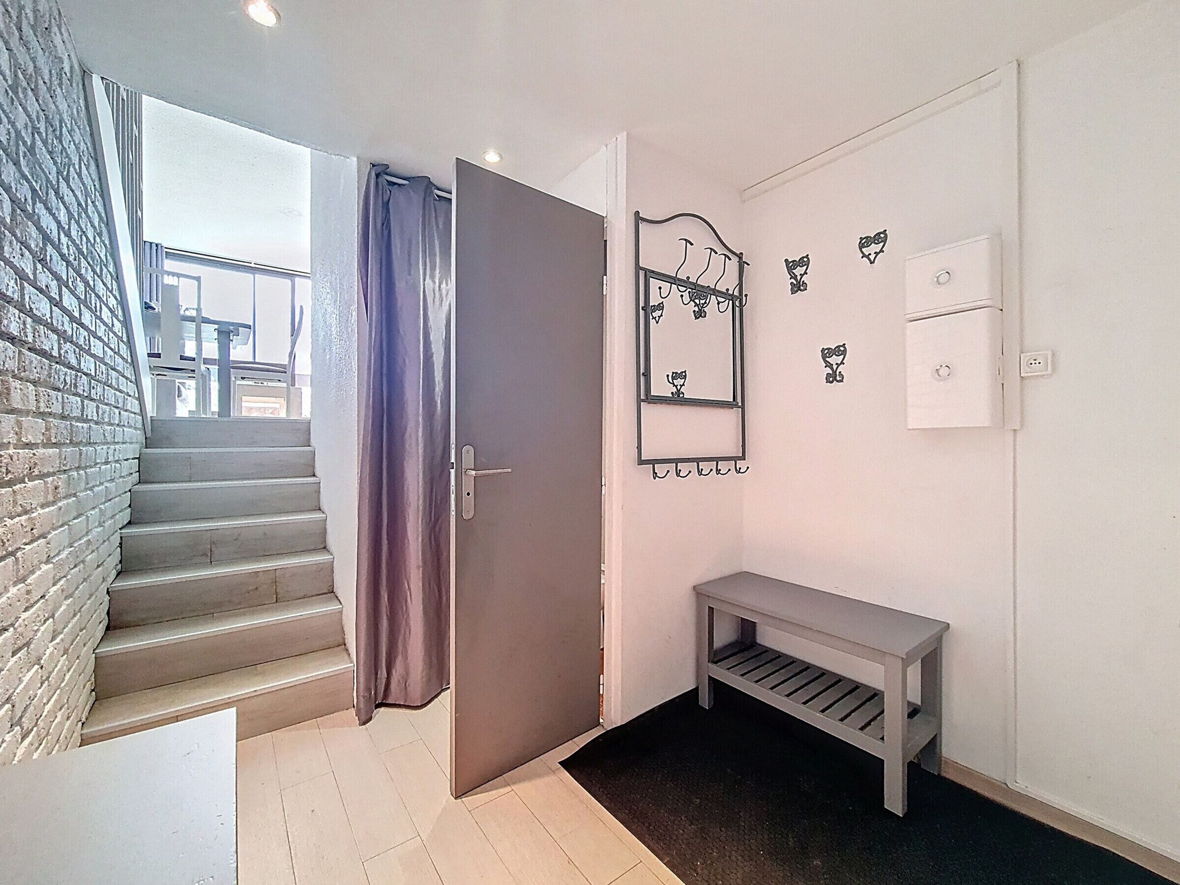 A staircase leading to a landing with a grey door, a bench, and a wall-mounted mirror with decorative elements.