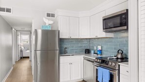 A modern kitchen with white cabinets, a stainless steel refrigerator, a microwave, an oven, and a kettle. - Golden Shores Penthouse (Ocean City)