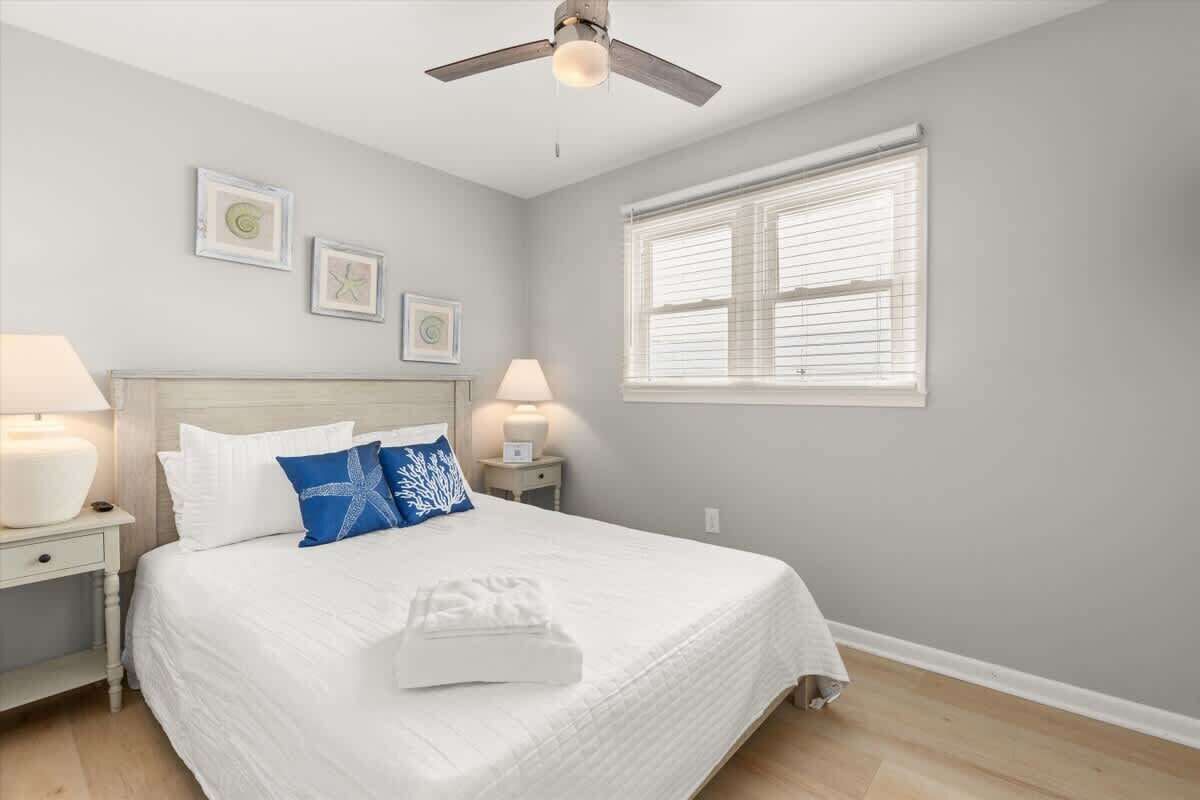A bedroom with a bed, two bedside tables with lamps, a ceiling fan, and a window with blinds.