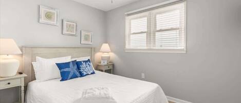 A bedroom with a bed, two bedside tables with lamps, a ceiling fan, and a window with blinds.