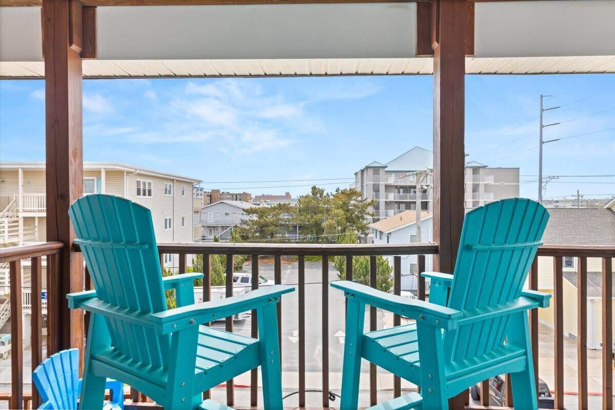 A balcony with two turquoise Adirondack chairs, a wooden railing, and a view of residential buildings.
