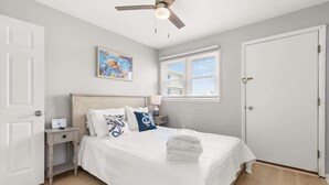 A bedroom with a bed, a nightstand, a ceiling fan, a window with blinds, and a door. - Golden Shores Penthouse (Ocean City)