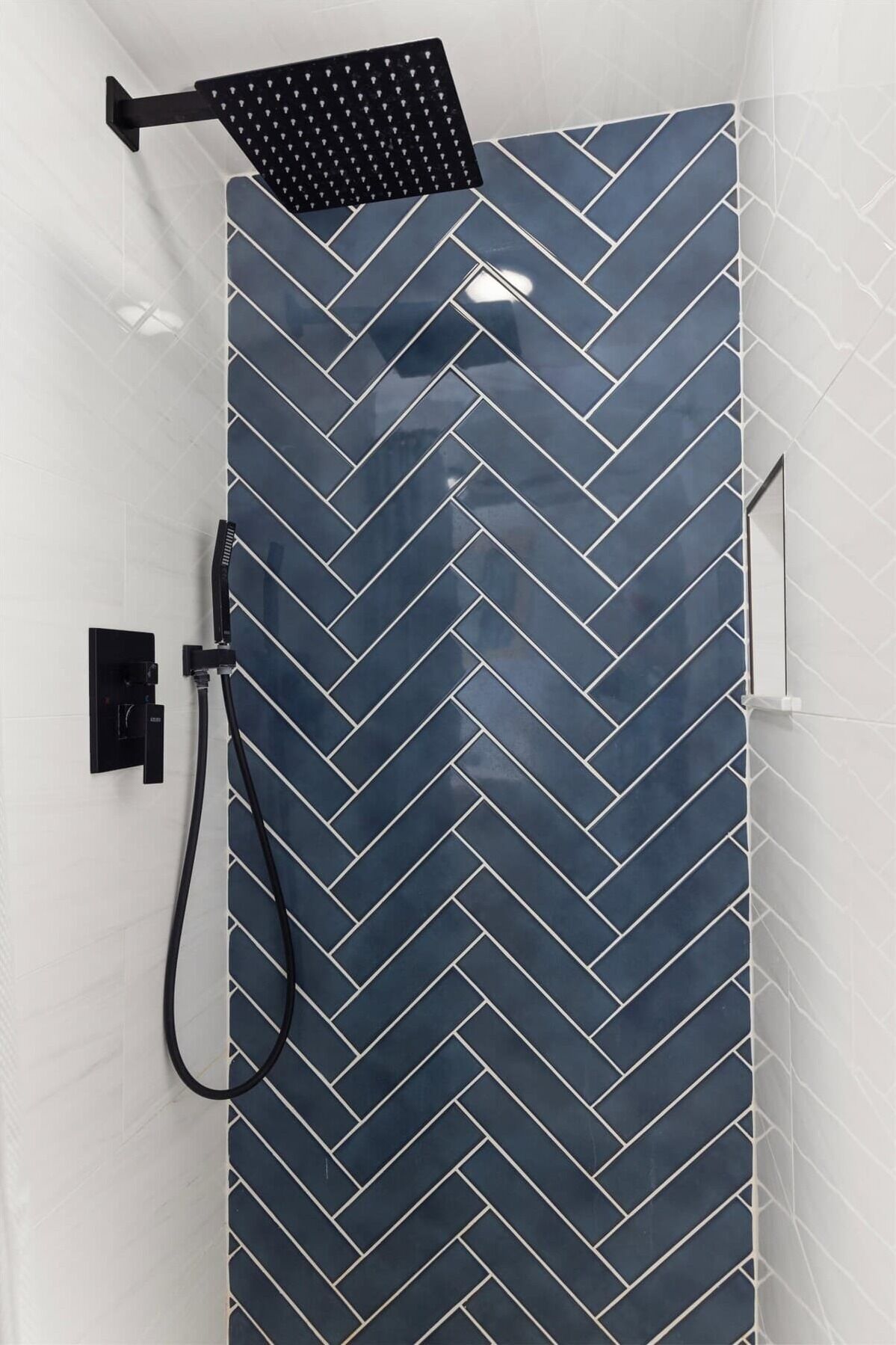Une douche avec un carrelage à motifs en chevrons, une douchette à main et un panneau de commande.