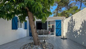 A courtyard with a tree, a table, and chairs, and a building with blue shutters and a white wall. - 4-room house near the sea with WIFI and pets allowed (La Palmyre)