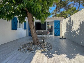 Ein Innenhof mit Baum, Tisch und Stühlen, sowie ein Gebäude mit blauen Fensterläden und einer weißen Wand.
