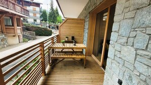 Une terrasse en bois avec une table et des bancs, des murs en pierre et un balcon donnant sur un quartier résidentiel.