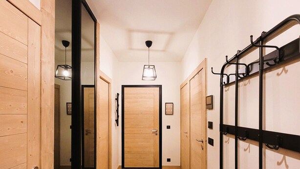 Un couloir avec des portes en bois, un banc et un porte-manteau.