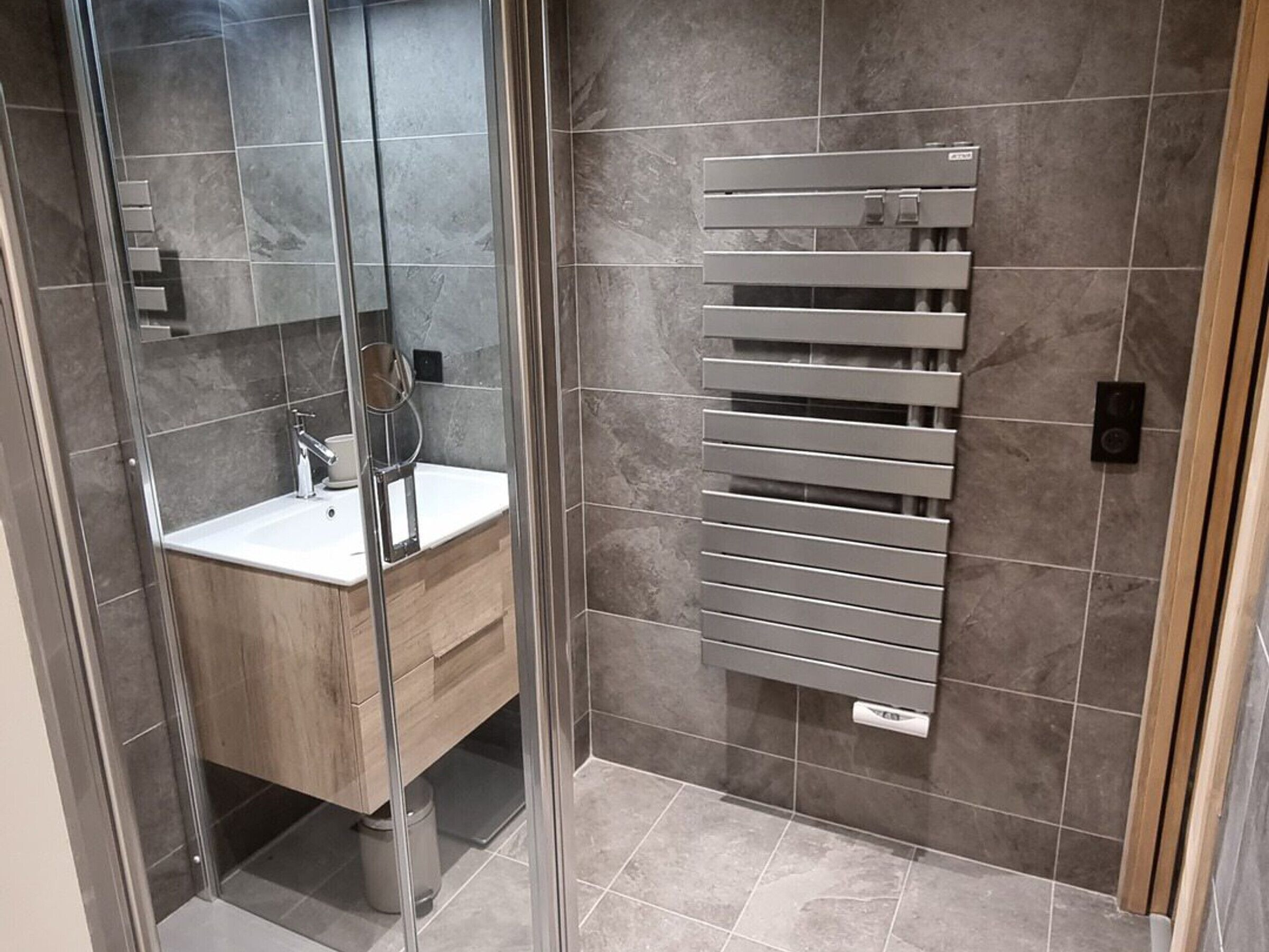 A modern bathroom with a glass shower enclosure, a wooden vanity, and a built-in towel rack.