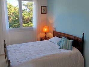 A bedroom with a bed, a nightstand, a lamp, a window, and a framed picture on the wall.