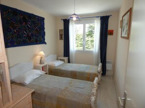 Une chambre avec deux lits, une fenêtre avec des rideaux, une tapisserie murale et un radiateur fixé au mur.