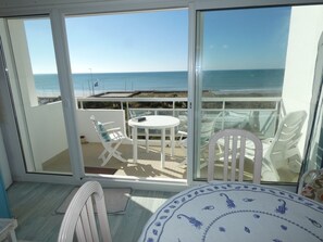Un balcon avec une table et des chaises, une vue sur la mer et une porte-fenêtre donnant sur l’extérieur.