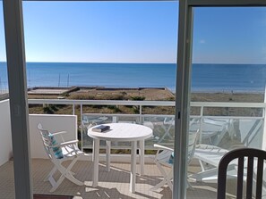 Un balcon avec une table et des chaises blanches, donnant sur une plage et l’océan.