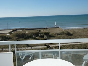 A coastal view from a balcony with a clear sky, a sandy beach, and a few sailboats.