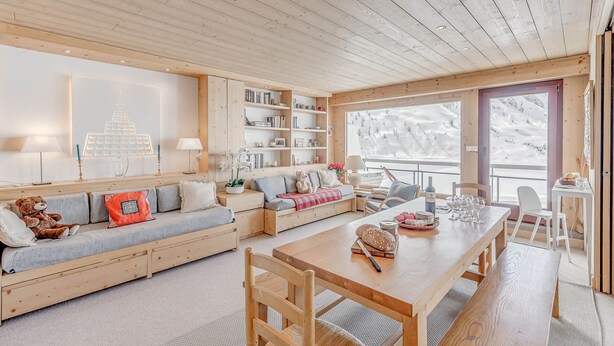 L’intérieur chaleureux d’un chalet avec un plafond en bois, un ensemble de canapés, une table à manger et une bibliothèque.